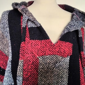 Könnte beinhalten: Ein Kapuzenponcho mit einem schwarz-rot-weiß gestreiften Muster. Der Poncho ist aus einem weichen, gewebten Stoff gefertigt.