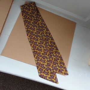 May include: A yellow necktie featuring a paisley design in red and white. The tie is made of a smooth material and is displayed on a brown surface. A classic accessory for formal or business wear.