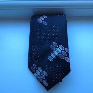 May include: A navy blue tie featuring a pattern of white and pink floral motifs and white polka dots. The tie is made of a smooth fabric, suitable for formal or business wear. The tie is approximately 147 cm in length.