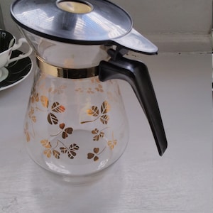 50er Jahre Pyrex-Krug, goldfarbenes Kleeblatt-Design, schwarzer, leicht zu fassender Kunststoffgriff, Daumen öffnen / schließen, Sirup- / Milch- / Saftausgießer.