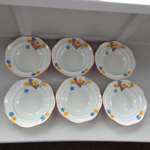 Peut inclure: Six bols en céramique blancs aux bords festonnés. Chaque bol présente un motif floral avec des accents jaunes, bleus et rouges. Les bords sont soulignés en orange. Un ensemble classique pour servir des soupes ou des desserts.