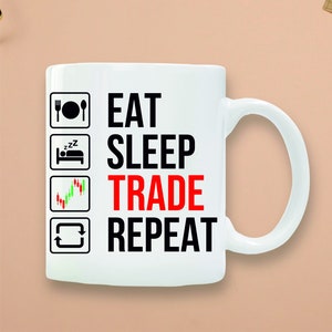 May include: White ceramic mug with the words "EAT SLEEP TRADE REPEAT" in black and red text. The mug features icons of a fork and plate, a bed, a stock chart, and a recycling symbol. The mug has a white handle.