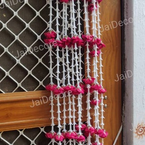 May include: Two white strings of artificial flowers with pink roses hanging on a wooden door with a white metal screen. The flowers are arranged in a cascading pattern.
