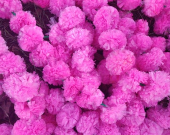 May include: A close-up of a large arrangement of pink tissue paper flowers. The flowers are arranged in a cluster and are all the same size and shape.