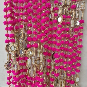 Puede incluir: Un cortina de puerta decorativa rosa y dorada con pequeños pompones y espejos redondos.