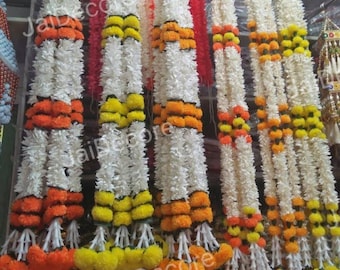May include: A collection of white flower garlands with orange and yellow accents. The garlands are hanging from a rack and are made of artificial flowers.