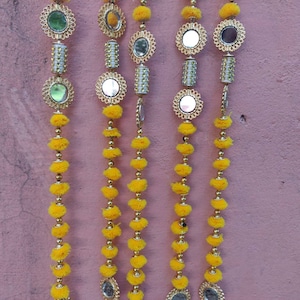 Puede incluir: Cuatro hileras de guirnaldas de pompones amarillos con pequeños espejos redondos y detalles dorados.