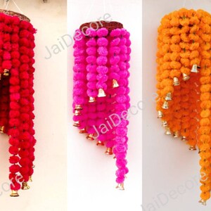 May include: Four hanging garlands of colorful pom-poms with bells. The garlands are yellow, red, pink, and orange. Each garland is made of multiple layers of pom-poms and has a wooden ring at the top.