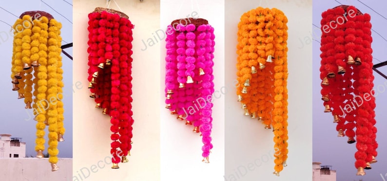 May include: Four hanging garlands of colorful pom-poms with bells. The garlands are yellow, red, pink, and orange. Each garland is made of multiple layers of pom-poms and has a wooden ring at the top.