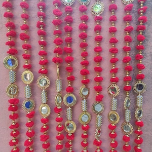 Puede incluir: Una cadena de pompones rojos con pequeños espejos redondos y detalles dorados. Los espejos están enmarcados en oro y tienen un diseño decorativo.