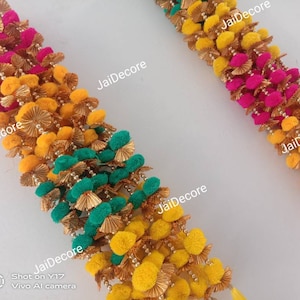 Puede incluir: Dos hileras de guirnalda de pompones coloridos con detalles dorados. La guirnalda está hecha de pompones rosas, amarillos y verdes. El texto "JaiDecore" aparece varias veces en la imagen.