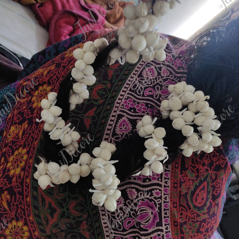 Pu&ograve; includere: Boccioli di fiori bianchi disposti in un motivo circolare, legati insieme con uno spago, e utilizzati come accessori per capelli. I boccioli di fiori sono disposti in un motivo circolare e legati insieme con uno spago. I boccioli di fiori sono bianchi e hanno una superficie leggermente ruvida.