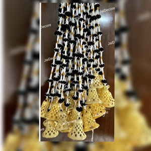 Puede incluir: Una larga guirnalda de pompones negros y blancos con cascabeles dorados que cuelgan de la parte inferior. La guirnalda está decorada con cuentas doradas y tiene el texto "JaiDecor" impreso.