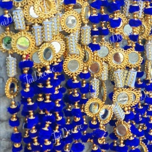 Puede incluir: Primer plano de guirnaldas decorativas azules y doradas ornamentadas. Cada hebra presenta adornos dorados, pequeños espejos y borlas azules vibrantes. El diseño es intrincado y detallado, con un enfoque en la textura y el color.