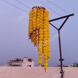 May include: A long garland of yellow marigold flower pom-poms with gold bells hanging from a metal pole.