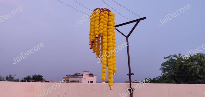 May include: A long garland of yellow marigold flower pom-poms with gold bells hanging from a metal pole.