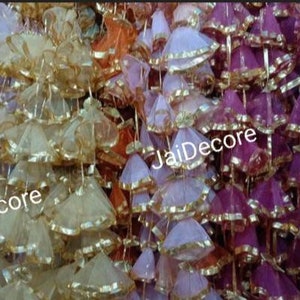 May include: A close-up of a variety of colorful fabric tassels with gold trim. The tassels are arranged in rows and are all hanging from a string. The tassels are made of a sheer fabric and have a ruffled appearance. The text "JaiDecor" is visible on the tassels.