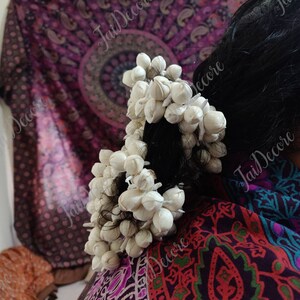 Pu&ograve; includere: Due fermagli per capelli a forma di fiore bianco con piccoli fiori bianchi disposti in forma circolare. I fermagli per capelli sono nei capelli scuri di una donna.