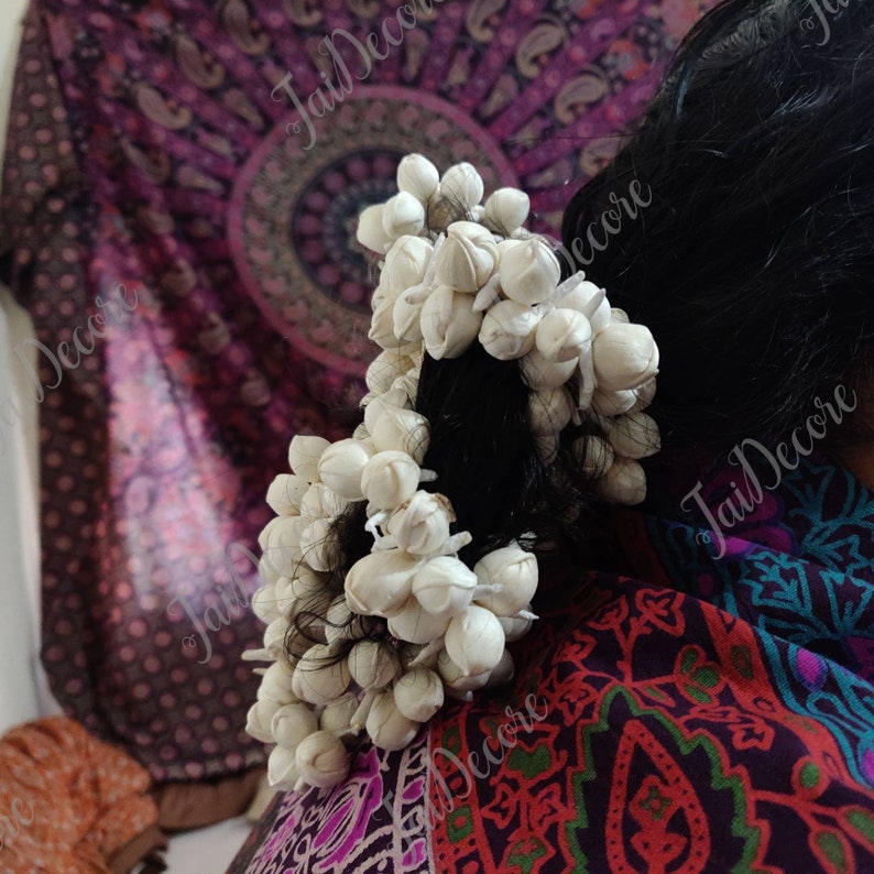 Pu&ograve; includere: Due fermagli per capelli a forma di fiore bianco con piccoli fiori bianchi disposti in forma circolare. I fermagli per capelli sono nei capelli scuri di una donna.