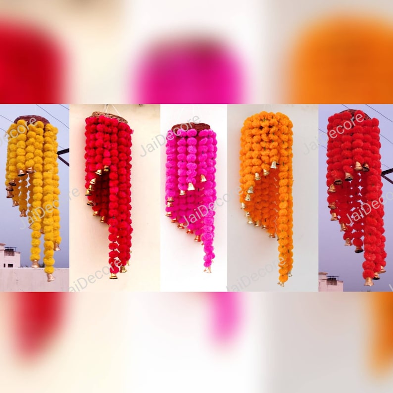 May include: Four hanging garlands of marigold flower pom-poms with bells. The garlands are yellow, orange, pink, and red.