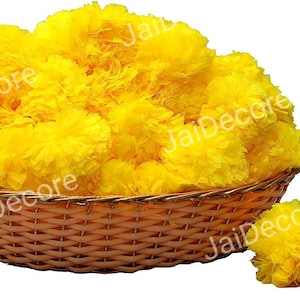 May include: A wicker basket filled with bright yellow marigold flower pom-poms. Two additional marigold pom-poms are on the table in front of the basket.
