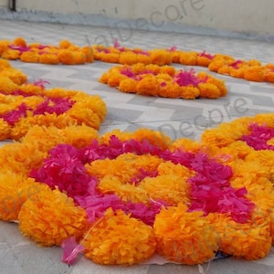 Op de afbeelding: Een decoratieve opstelling van gele en roze goudsbloemkransen op een betegelde vloer. De kransen zijn in een cirkelvormige opstelling geplaatst, wat een feestelijke en kleurrijke weergave creëert.