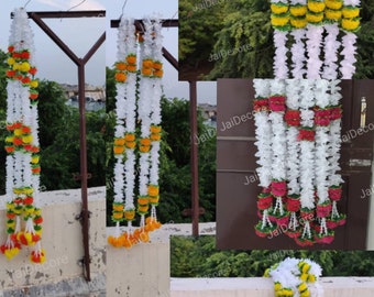 May include: Three strands of artificial flower garlands, each with white petals and a mix of yellow and orange or red flower centers. The garlands are hanging from a metal structure.