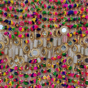 Puede incluir: Guirnaldas de pompones multicolores con pequeños espejos redondos y detalles dorados. Las guirnaldas están hechas de hilo de colores y están enhebradas con cuentas doradas.