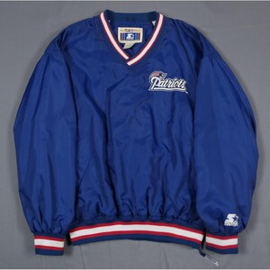 May include: A blue Patriots windbreaker jacket with a V-neck collar. The jacket features the Patriots logo on the chest and red and white striped trim on the cuffs and hem. The Starter logo is visible on the sleeve.