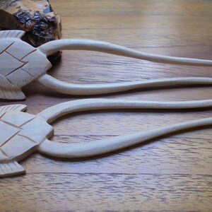 Puede incluir: Dos palos de pelo de madera con dise&ntilde;os de cabeza de tortuga. Los palos son de color marr&oacute;n claro y tienen un acabado liso.