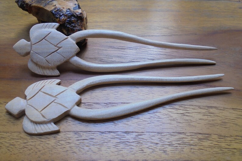 Puede incluir: Dos palos de pelo de madera con dise&ntilde;os de cabeza de tortuga. Los palos son de color marr&oacute;n claro y tienen un acabado liso.