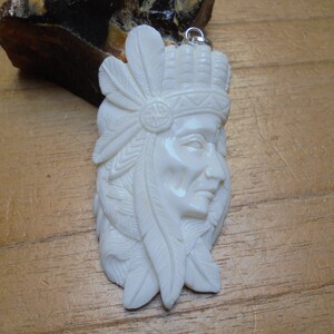 May include: White carved bone pendant of a Native American chief wearing a headdress with feathers. The pendant has a silver bail.