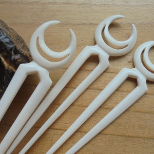 Puede incluir: Cuatro palitos para el pelo blancos con un diseño de luna creciente. Los palitos están hechos de hueso y tienen un acabado liso y pulido.