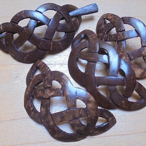 May include: Three brown coconut shell hair clips with a Celtic knot design. Each clip has a small wooden pin.