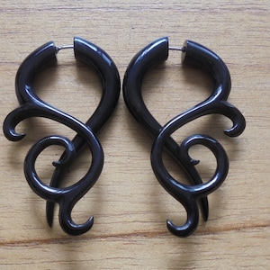 May include: A pair of black, ornate, wooden earrings with a swirl design. The earrings are made of dark wood and have a polished finish.