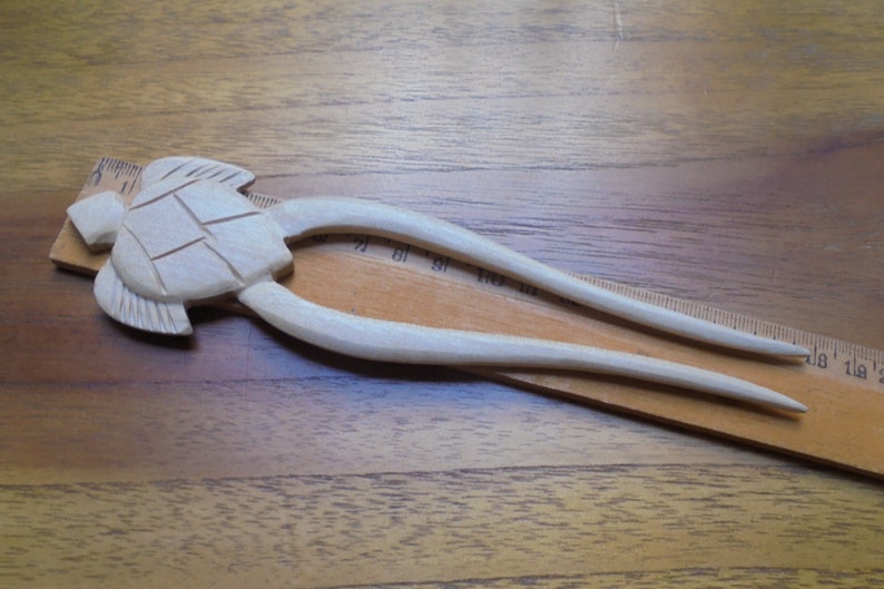 Puede incluir: Una horquilla para el pelo de madera con un dise&ntilde;o de tortuga tallada. La horquilla mide aproximadamente 15 cm de largo y est&aacute; hecha de madera clara.