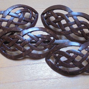 May include: Four brown coconut shell hair clips with a woven design. The clips are connected by a brown wooden stick.