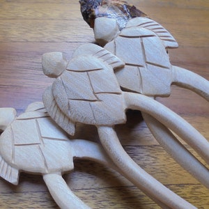 Puede incluir: Conjunto de tres palitos para el pelo de madera con dise&ntilde;os de tortugas talladas. Los palitos son de color marr&oacute;n claro y las tortugas son de un tono marr&oacute;n ligeramente m&aacute;s claro.