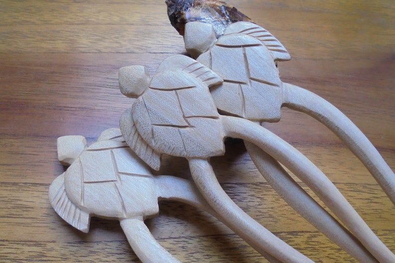 Puede incluir: Conjunto de tres palitos para el pelo de madera con dise&ntilde;os de tortugas talladas. Los palitos son de color marr&oacute;n claro y las tortugas son de un tono marr&oacute;n ligeramente m&aacute;s claro.