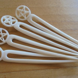 May include: Set of five white hair sticks with a five-pointed star design at the top.