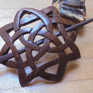 May include: A brown wooden hair stick with a carved Celtic knot design. The stick is about 6 inches long and has a smooth finish.