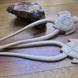Puede incluir: Dos palos de pelo de madera con dise&ntilde;os de cabeza de tortuga. Los palos son de color marr&oacute;n claro y las tortugas est&aacute;n talladas en detalle.