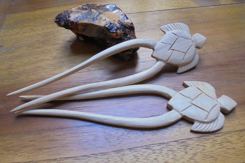 Puede incluir: Dos palos de pelo de madera con dise&ntilde;os de cabeza de tortuga. Los palos son de color marr&oacute;n claro y las tortugas est&aacute;n talladas en detalle.