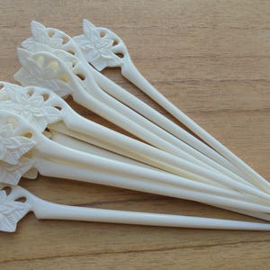 May include: A set of eight white hair sticks with floral designs. The sticks are made of a smooth, polished material and have a delicate, feminine look.