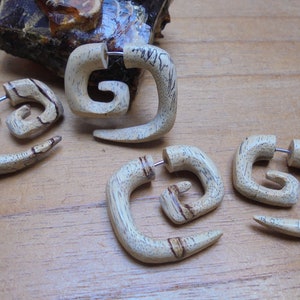 May include: Four wooden spiral ear gauges, each with a different wood grain pattern. The gauges are a light brown color and have a silver metal post.