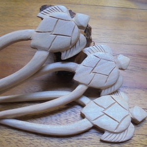 Puede incluir: Tres palitos de pelo de madera con dise&ntilde;os de tortugas talladas. Los palitos son de color marr&oacute;n claro y las tortugas est&aacute;n detalladas con un caparaz&oacute;n texturizado.
