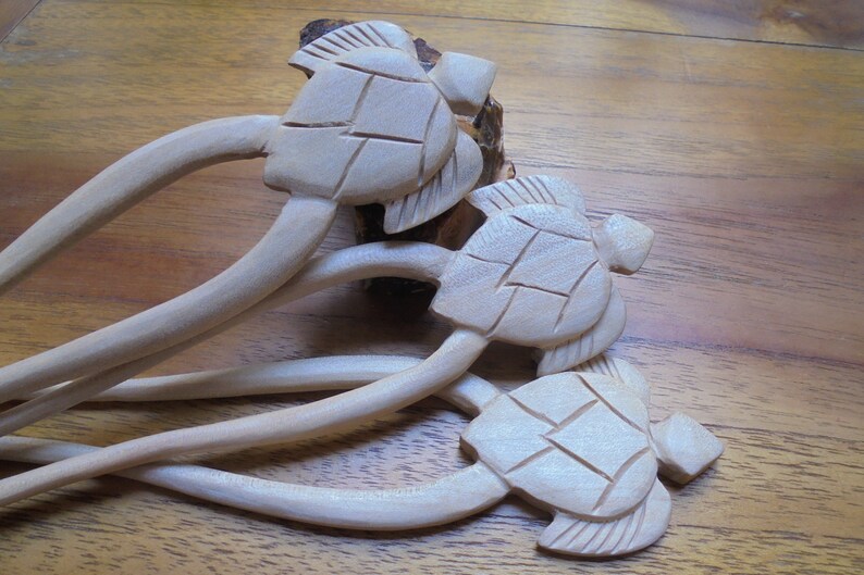 Puede incluir: Tres palitos de pelo de madera con dise&ntilde;os de tortugas talladas. Los palitos son de color marr&oacute;n claro y las tortugas est&aacute;n detalladas con un caparaz&oacute;n texturizado.