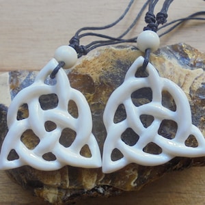 May include: Two white Celtic knot pendants on black cords with white beads. The pendants are carved in a triangular shape with intricate knot designs.