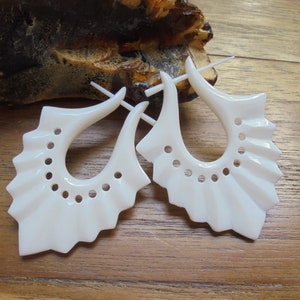Puede incluir: Un par de pendientes de hueso blanco con un diseño único en forma de abanico y un pequeño agujero en el centro de cada pendiente.