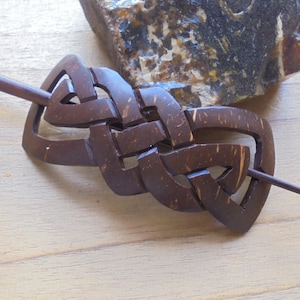 May include: A brown wooden hair stick with a Celtic knot design. The stick is made of coconut wood and has a natural finish.